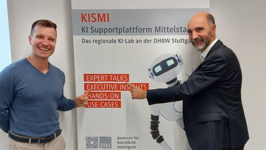 Dr. Christian Tutschku vom Fraunhofer IAO und Prof. Dr. Dirk Reichhardt von der DHBW Stuttgart vor dem Plakat der Veranstaltung