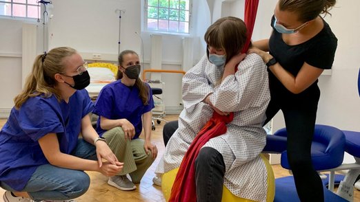 Vier Teilnehmerinnen beim Simulationstraining - Eine Teilnehmerin spielt dabei die Gebärende und sitzt auf einem Hocker..