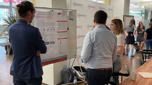 Posterpräsentation - Mehrere Personen schauen sich eines der Poster an.