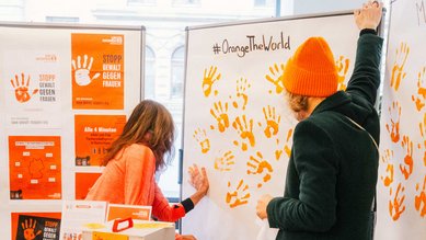 Besucherin hinterlässt einen orangefarbenen Handabdruck auf der dafür vorgesehenen Papierwand.