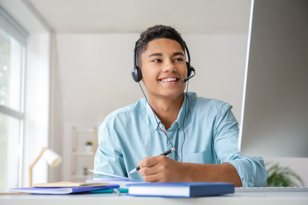 Ein lachender Student mit Headset sitzt vor einem Bildschirm.