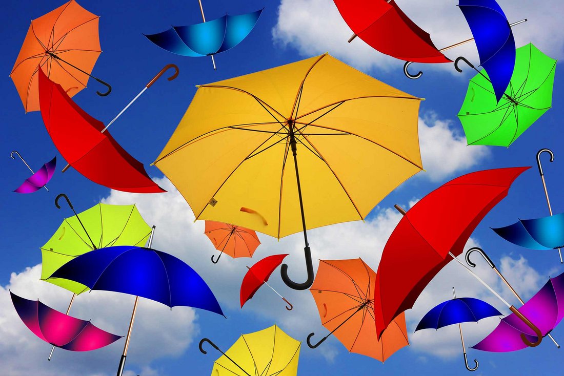 Verschiedenfarbige Regenschirme vor einem blauen Himmel mit weißen Wolken