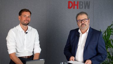 Maximilian Wäger, mit weißem Hemd und Prof. Dr. Sven Köhler, in weißem Hemd und blauem Sakko, sitzen vor einem grauen Hintergrund und schauen in die Kamera..