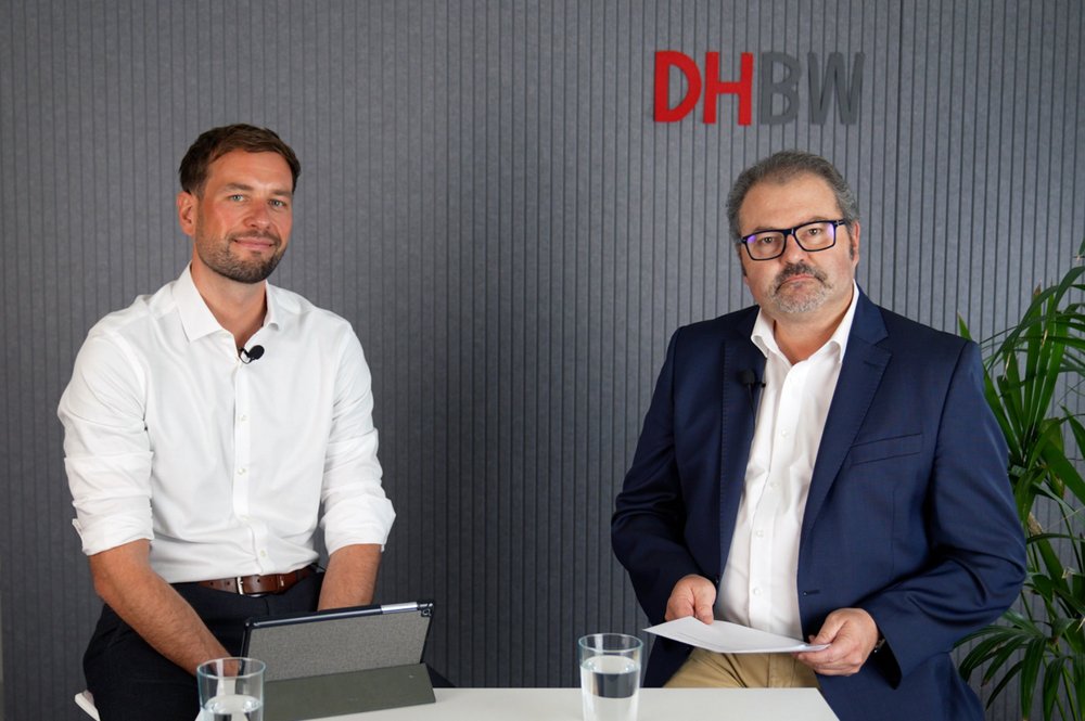 Maximilian Wäger, mit weißem Hemd und Prof. Dr. Sven Köhler, in weißem Hemd und blauem Sakko, sitzen vor einem grauen Hintergrund und schauen in die Kamera..