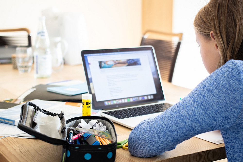 Junge Frau sitzt am Schreibtisch und schaut auf den Bildschirm ihres Laptops.