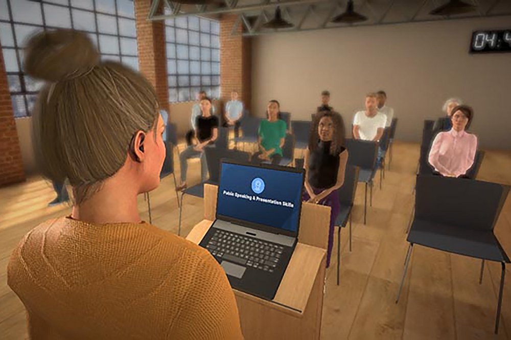 Eine Person steht an einem Podium und spricht zu einem Publikum, das in Reihen von Stühlen sitzt. Die Person am Podium benutzt einen Laptop, auf dem der Text "Public Speaking & Presentation Skills" angezeigt wird. Das Publikum besteht aus mehreren Personen, die aufmerksam zuhören. Der Raum hat große Fenster und freiliegende Ziegelwände, was ihm ein industrielles Flair verleiht. An der Wand hängt eine digitale Uhr, die die Zeit "04:46" anzeigt.