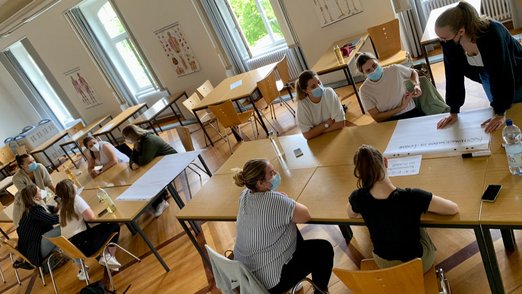 Teilnehmerinnen sitzen in einem großen Raum an Tischen.