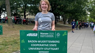 Elena Holm, die ein grünes Schild mit der Aufschrift "Baden-Wuerttemberg Cooperative State University Stuttgart, Germany" vor sich hält. 