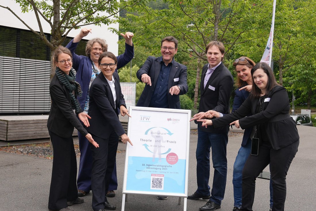 Gruppenbild, auf dem alle auf das in der Mitte stehende Plakat der Tagung zeigen. 