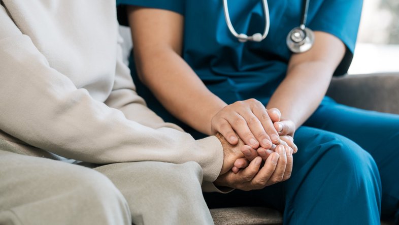 Ethik im Gesundheitswesen Eine Krankenschwester hält die Hand einer Patientin.