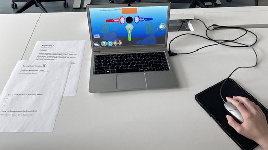 Aufgeklappter Laptop, auf dessen Bildschirm die passende Farbe gefunden werden muss.