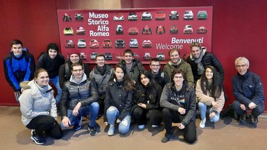 Die Studierendengruppe um Prof. Dr. Christian Götz Gruppenbild vor einem Plakat des Museo Storico Alfa Romeo