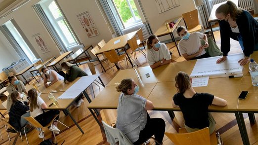 Teilnehmerinnen sitzen in einem großen Raum an Tischen.