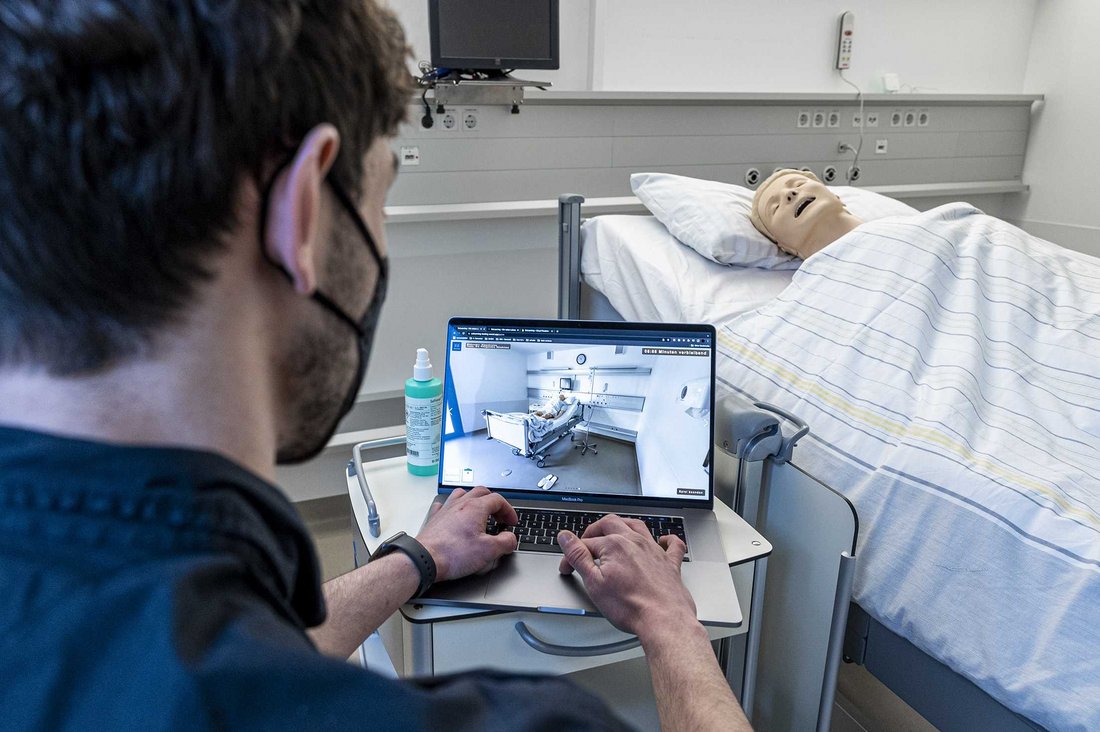 Blick über die Schulter eines Studierenden auf einen Bildschirm und ein Patientenbett im Simulationszentrum „STUPS“ des Klinikums Stuttgart. 