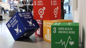 Verschiedenfarbige Würfel-Elemente, die mit Sustainable Development Goals (SDGs) der UN bedruckt sind. 