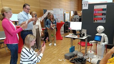 Highlight am ZDT-Stand am Tag der Lehre in Mosbach: der humanoide Roboter Pepper Roboter Pepper wird von mehreren Besuchenden am Messestand des ZDT mit dem Smartphone fotografiert.