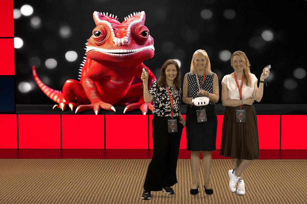 Ilona Hoppe, Prof. Dr. Margrit Ebinger und Michaela Riester stehen vor einem schwarzen Hintergrund mit Lichtflecken, auf dem ein rotes Chamäleon zu sehen ist, das auf roten Blöcken sitzt.