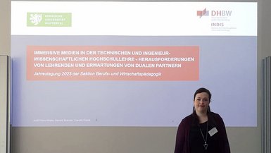 Judit Klein-Wiele präsentierte den aktuellen Stand ihres kooperativen Promotionsvorhabens. Judit Klein-Wiele steht vor einer auf die Wand projizierten Folie mit dem Titel ihrer Arbeit.